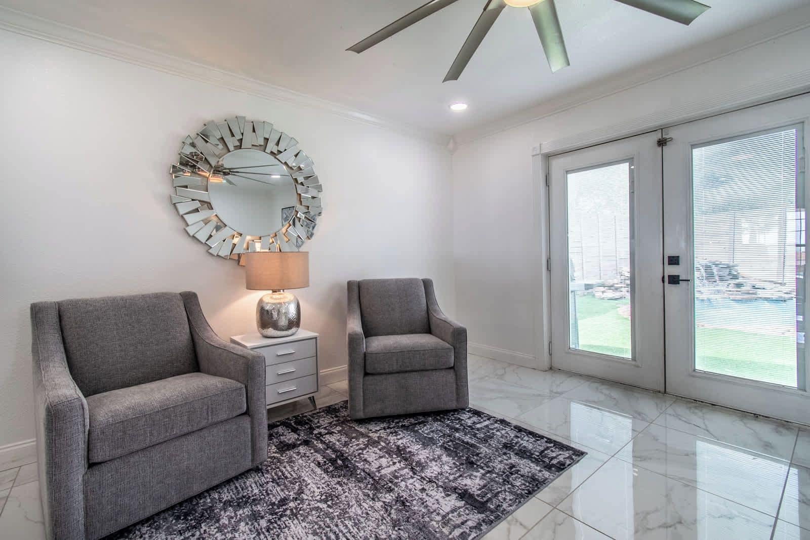 A modern interior with two armchairs, a side table, a lamp, and a large mirror.