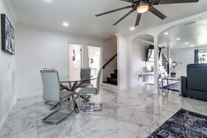 A modern interior with a dining area featuring a glass table and chairs, a ceiling fan, and a staircase leading to another level. - Ocean Drive Splendor Awaits (Corpus Christi)
