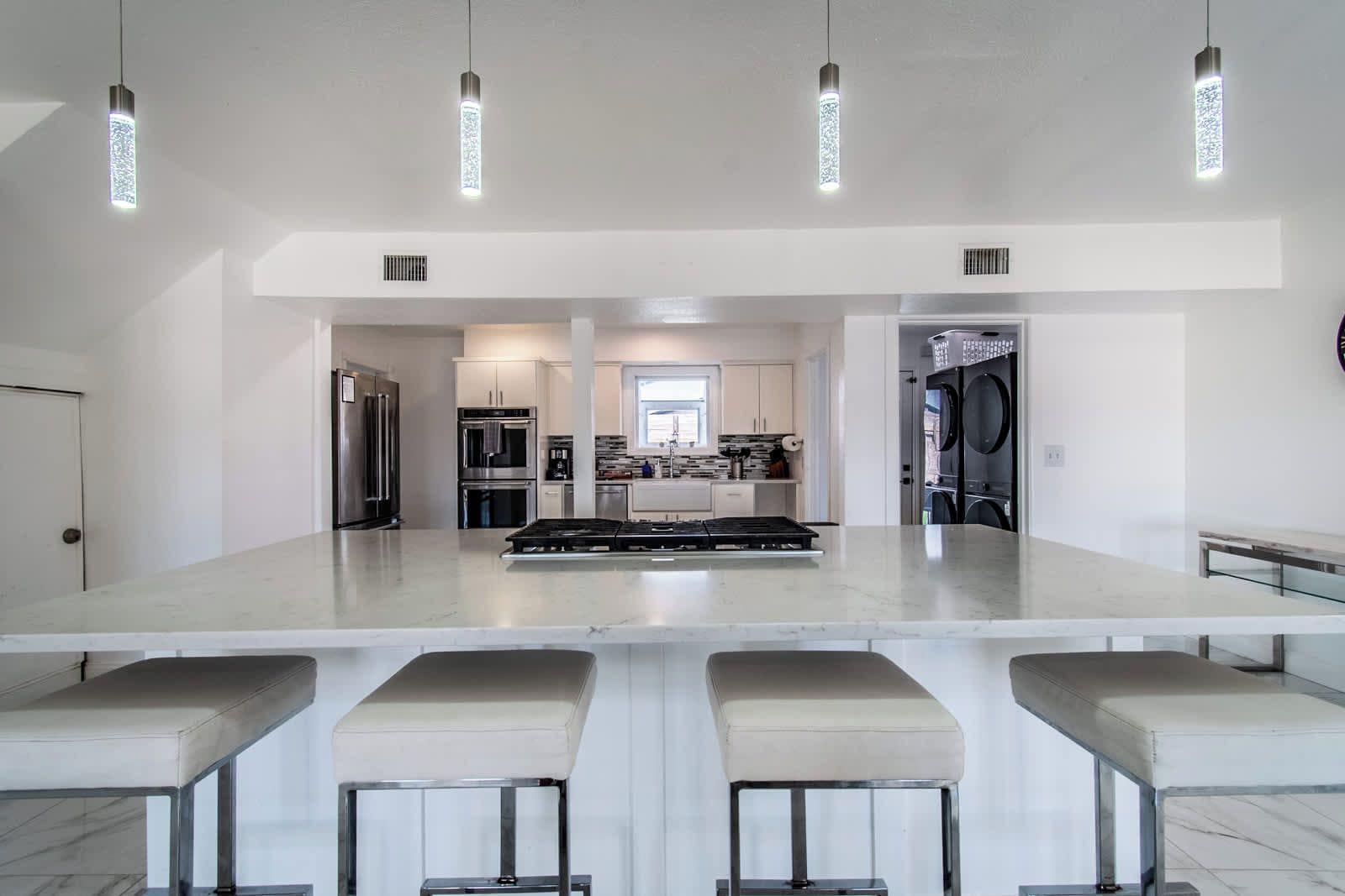 A modern kitchen with a central island, bar stools, stainless steel appliances, and pendant lighting.