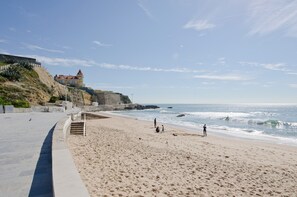 Ein Strand mit einer Steinmauer, einem Gebäude mit rotem Dach und Wellen im Hintergrund.