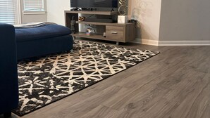 Un salon avec un téléviseur à écran plat, un canapé bleu, un tapis à motifs et un plancher en bois.