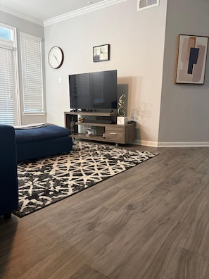 Ein Wohnzimmer mit Flachbildfernseher, einem blauen Sofa, einem gemusterten Teppich und Holzboden.