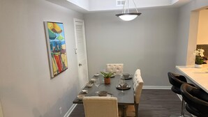 Un coin repas avec une table dressée pour quatre personnes, des chaises, une suspension et un tableau au mur.