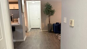 Un couloir avec un plancher en bois, une porte blanche, une plante en pot et un canapé bleu.