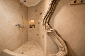 A shower with a curved wall design, a small shelf with a plant and a bottle, and a wooden texture on the wall. - Mykonos Sunday Home Costa Ilios (Mykonos)