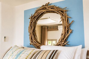 A room with a circular woven wall decoration, a bed with striped pillows, and a visible door in the background. - Mykonos Sunday Home Costa Ilios (Mykonos)