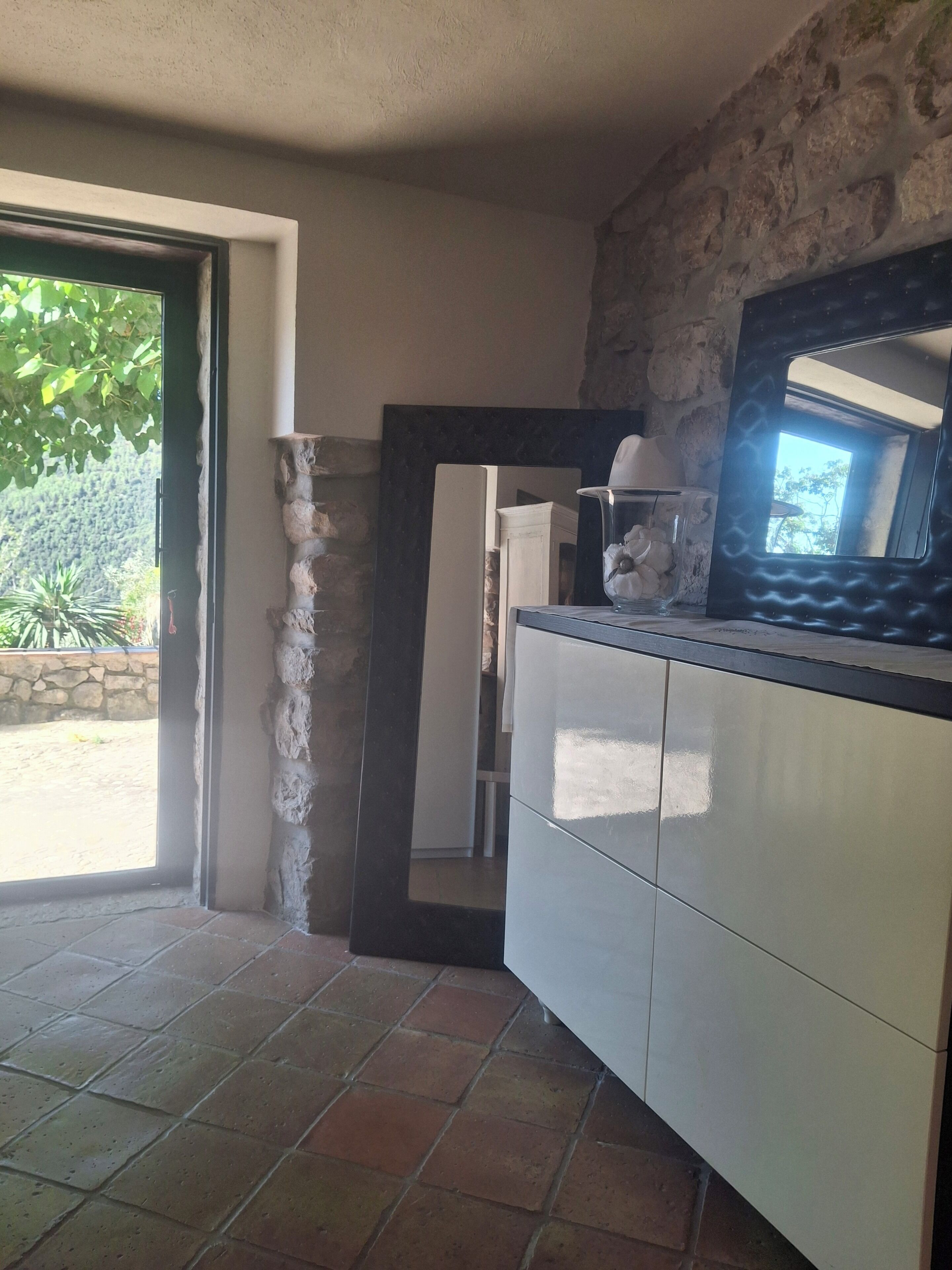 A kitchen with a stone wall, a tiled floor, and a view of greenery outside.