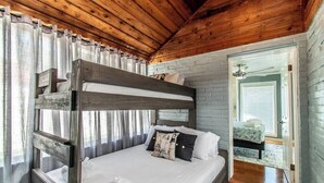 A bunk bed with a wooden headboard, white bedding, and a pillow with a vintage design. - Ocean View + Poolside Opulence Tennis (Corpus Christi)