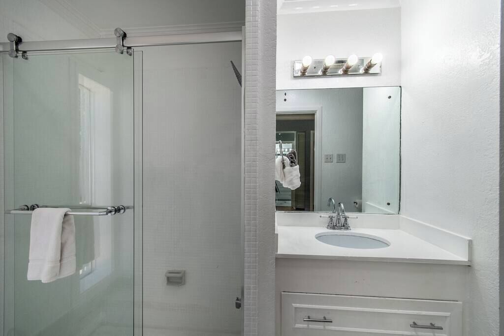 A bathroom with a glass shower door, a white sink with a mirror above it, and a towel rack.