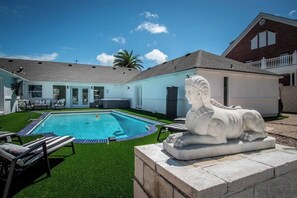 Piscina com espreguiçadeiras, uma estátua e uma casa com varanda.