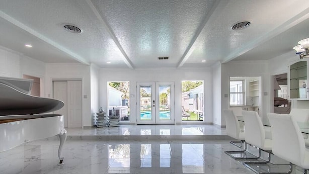 A spacious room with a piano, a pool view, and a dining area with chairs. - Ocean View + Poolside Opulence Tennis (Corpus Christi)