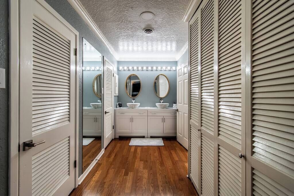 A hallway with wooden flooring, white cabinets, and a mirror.