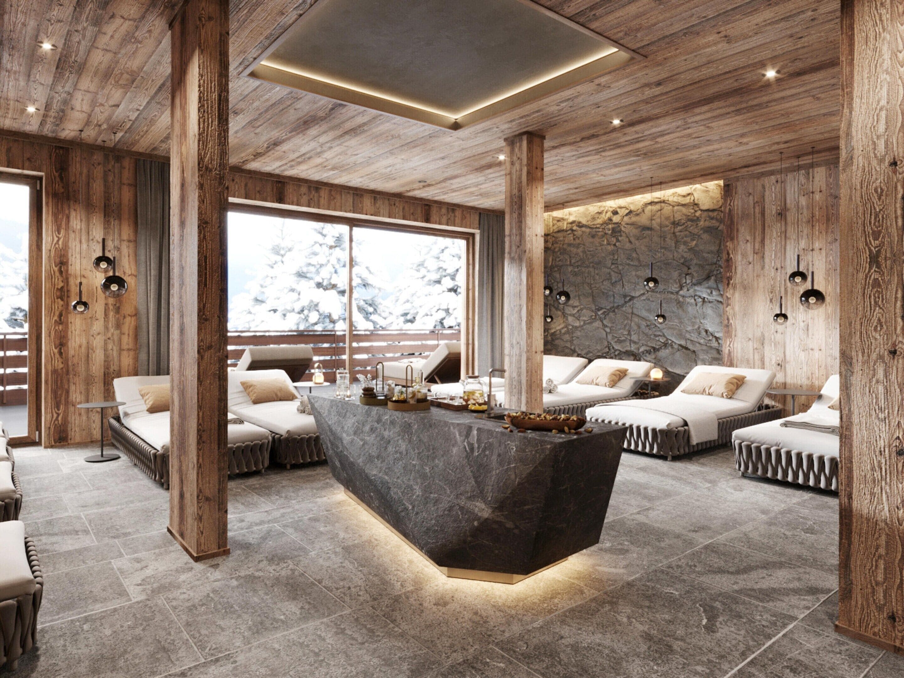 A modern interior with a central island, wooden beams, stone walls, and a view of snow-covered trees.