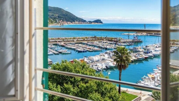 Un puerto deportivo con barcos amarrados, un cielo azul despejado y un paisaje montañoso al fondo.
