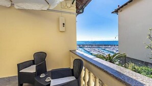 Un balcón con mobiliario de mimbre, vista al mar y un edificio de fachada blanca.