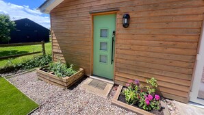 Eine Holzhütte mit grüner Tür, einer kleinen Veranda und erhöhten Blumenbeeten.