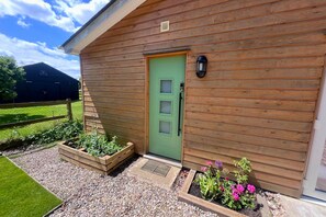 A wooden cabin with a green door, a small porch, and raised garden beds with flowers. - Moor View, Reepham, Norfolk (Reepham)