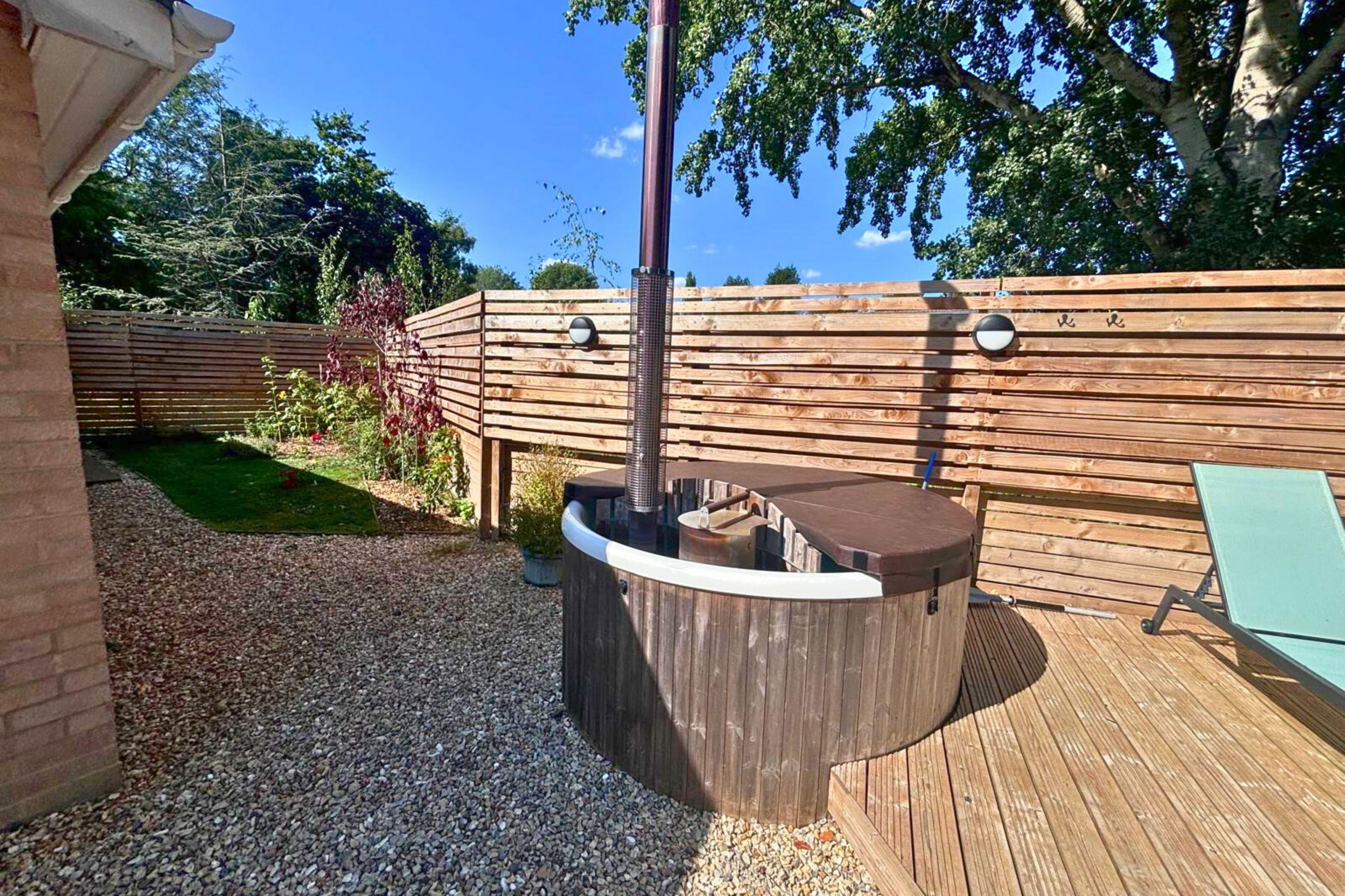 A hot tub with a wooden deck, surrounded by a wooden fence and greenery.