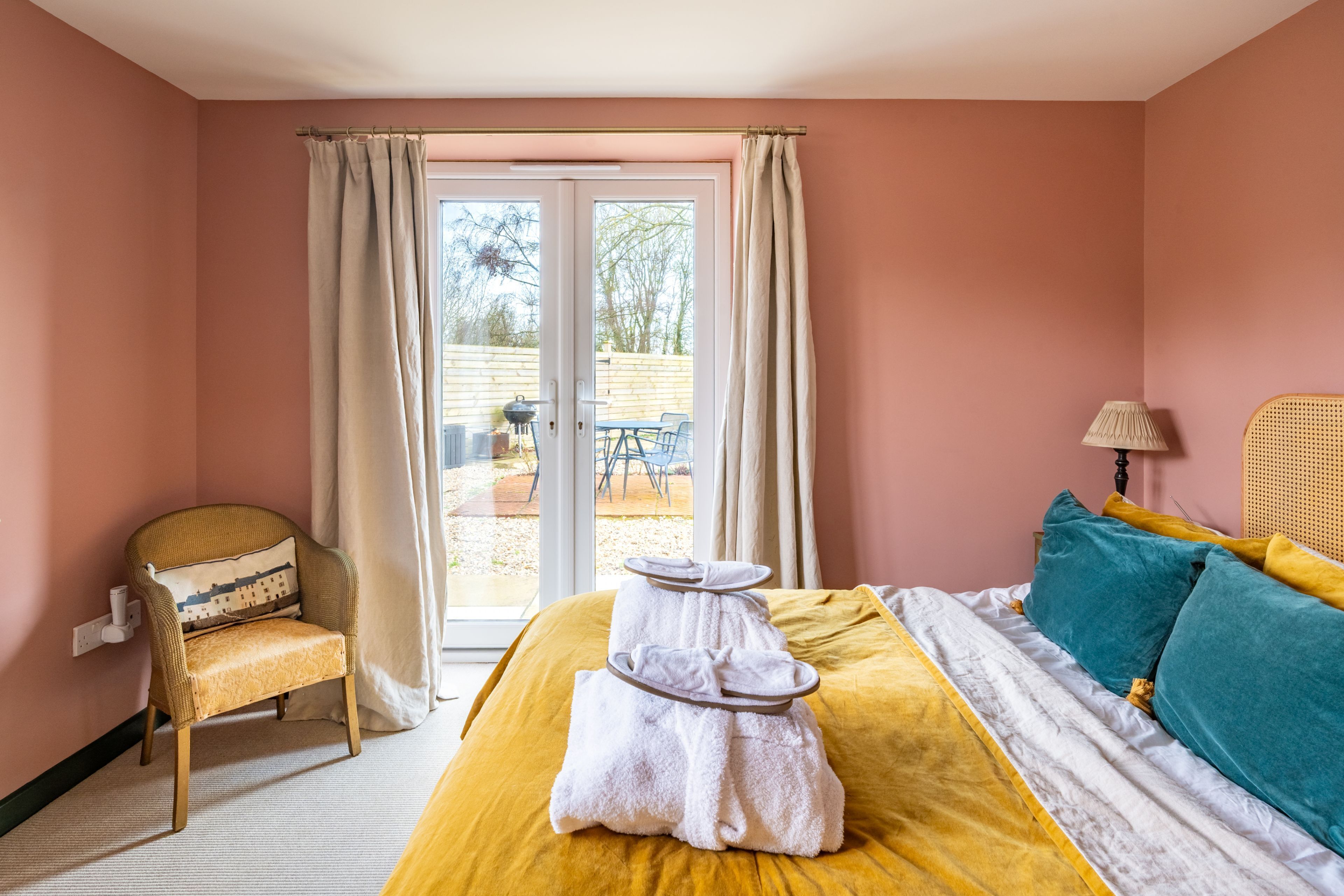 A bedroom with a bed, a chair, a table, and a view through a glass door.