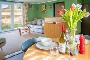 A dining area with a table set for two, a vase of flowers, wine bottles, and a red pepper mill. - Moor View, Reepham, Norfolk (Reepham)