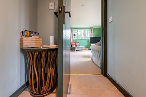 A hallway leading to a room with a bed, a TV, and a window with curtains. - Moor View, Reepham, Norfolk (Reepham)