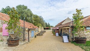 A cobblestone path leading to a row of traditional buildings with wooden shutters and potted plants. - Shammer Lodge, North Creake, Norfolk (North Creake)