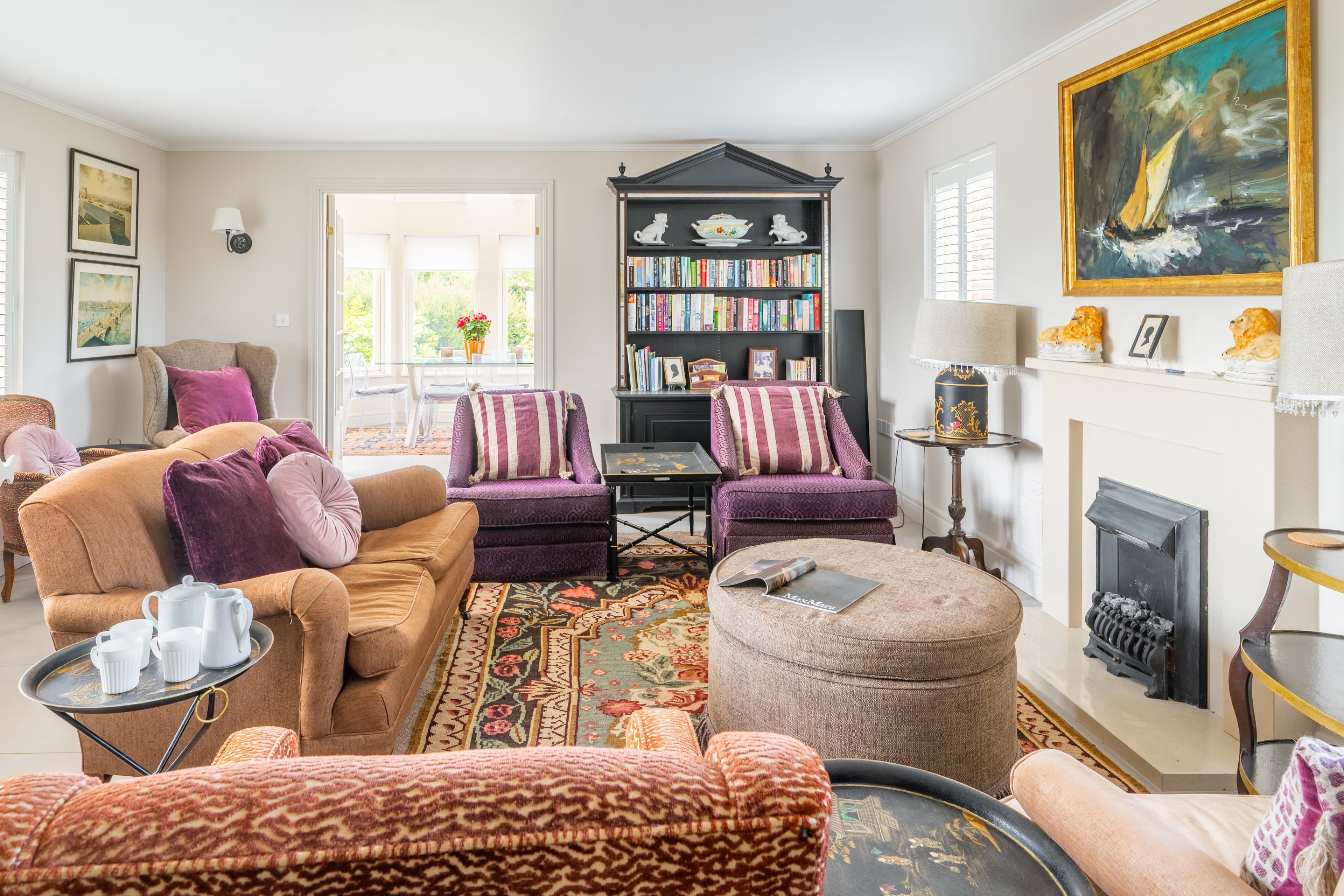 A living room with a sofa, armchairs, a fireplace, a bookshelf, and a painting.