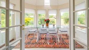 A conservatory with a glass table, four chairs, a patterned rug, and a potted plant with red flowers. - Shammer Lodge, North Creake, Norfolk (North Creake)