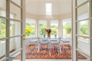 A conservatory with a glass table, four chairs, a patterned rug, and a potted plant with red flowers. - Shammer Lodge, North Creake, Norfolk (North Creake)