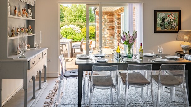A dining area with a table set for four, clear chairs, a buffet counter with glassware, and a view of the garden through glass doors. - Shammer Lodge, North Creake, Norfolk (North Creake)