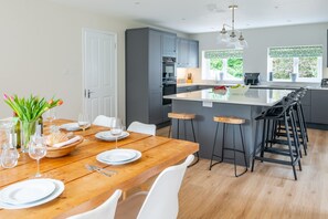 A modern kitchen with grey cabinets, a wooden dining table set for six, and a large island with bar stools. - Manor Farm Lodge, Brancaster, Norfolk (Brancaster)