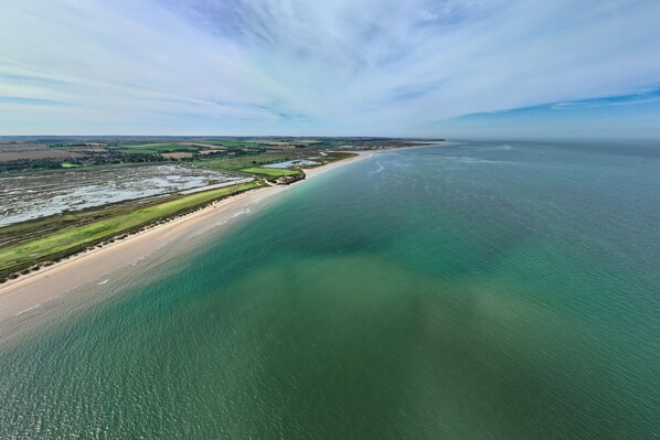 An aerial view of a coastal area with a beach, green fields, and a clear sky. - Manor Farm Lodge, Brancaster, Norfolk (Brancaster)
