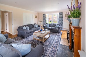 A living room with two grey sofas, a patterned rug, a wooden coffee table, and a large potted plant. - Manor Farm Lodge, Brancaster, Norfolk (Brancaster)