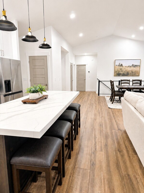 A modern kitchen with a large island, wooden flooring, and pendant lighting.