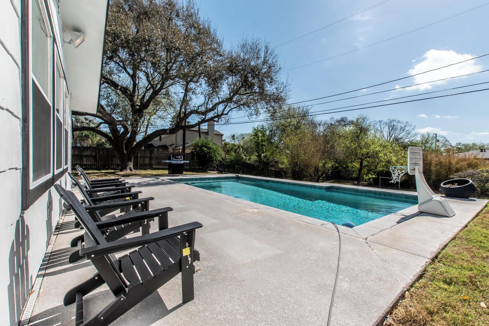 A swimming pool with lounge chairs, a basketball hoop, and a building in the background.