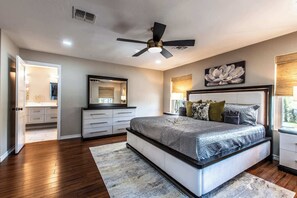 Ein Schlafzimmer mit Bett, Deckenventilator, Nachttisch, Lampe, Kommode und Fenster.