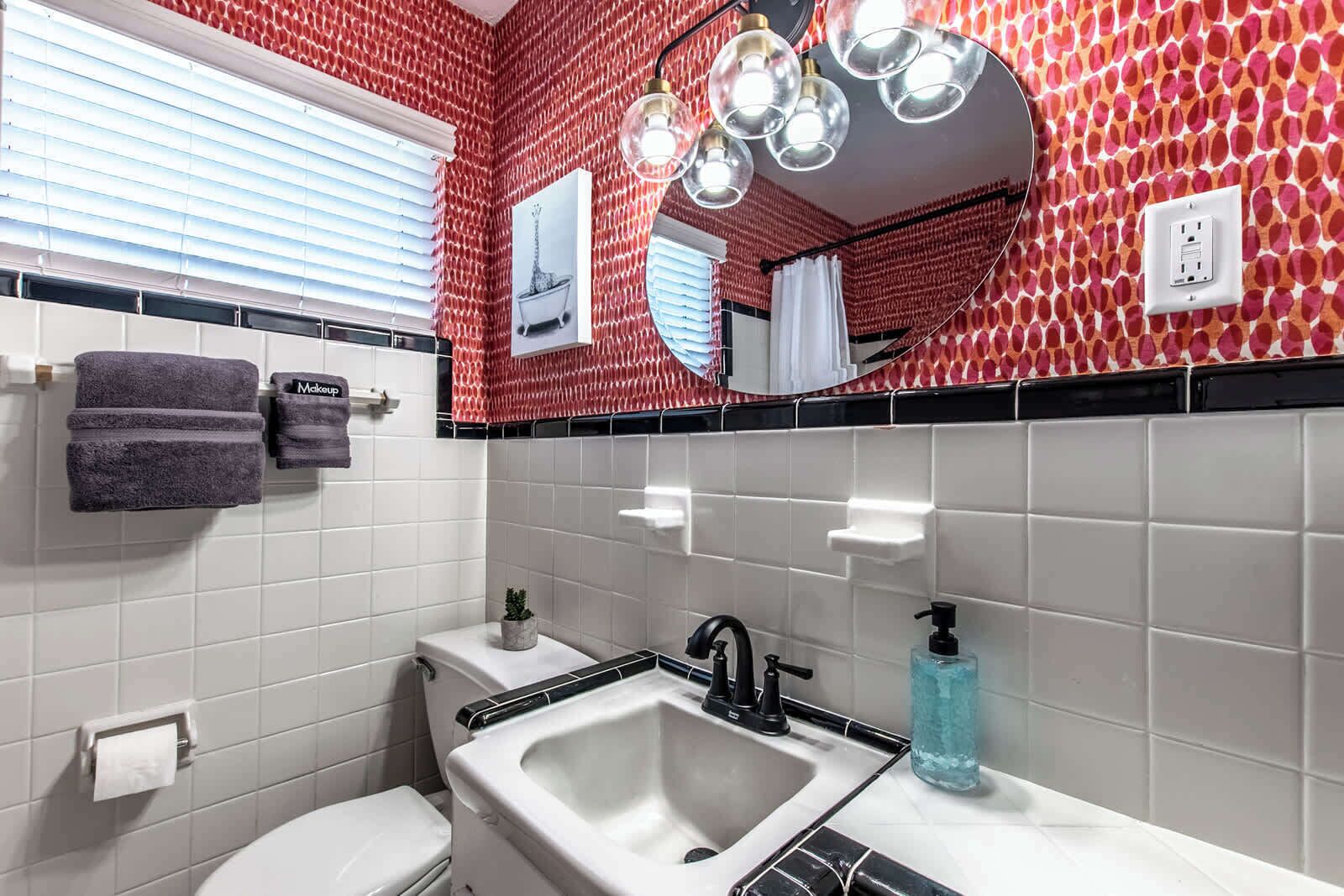 Ein Badezimmer mit roter Wand, einem Muster, einem weißen Waschbecken, einem Spiegel und einer Toilette.