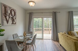 Un salon moderne avec une table à manger en verre, un canapé et une porte-fenêtre coulissante donnant sur une terrasse.
