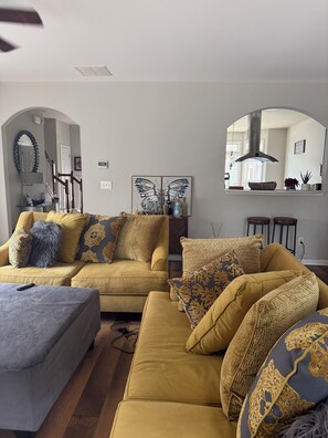 Un salon comprenant un ensemble de canapés, une table basse, un miroir et un élément décoratif représentant des papillons, fixé au mur.