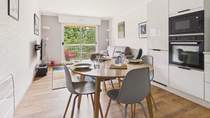 Eine moderne Küche mit weißen Schränken, einem Esstisch mit Stühlen und Blick durch eine Schiebetür auf einen Balkon.