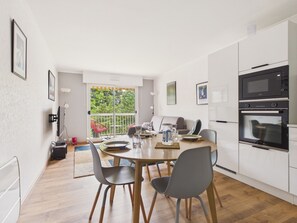 A modern kitchen with white cabinets, a dining table with chairs, and a view through a sliding glass door to a balcony. - 300m from beach, apt for 3 (Pornichet)