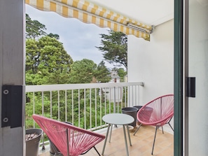 A balcony with a white railing, two red chairs, a small round table, and a yellow and white striped awning. - 300m from beach, apt for 3 (Pornichet)