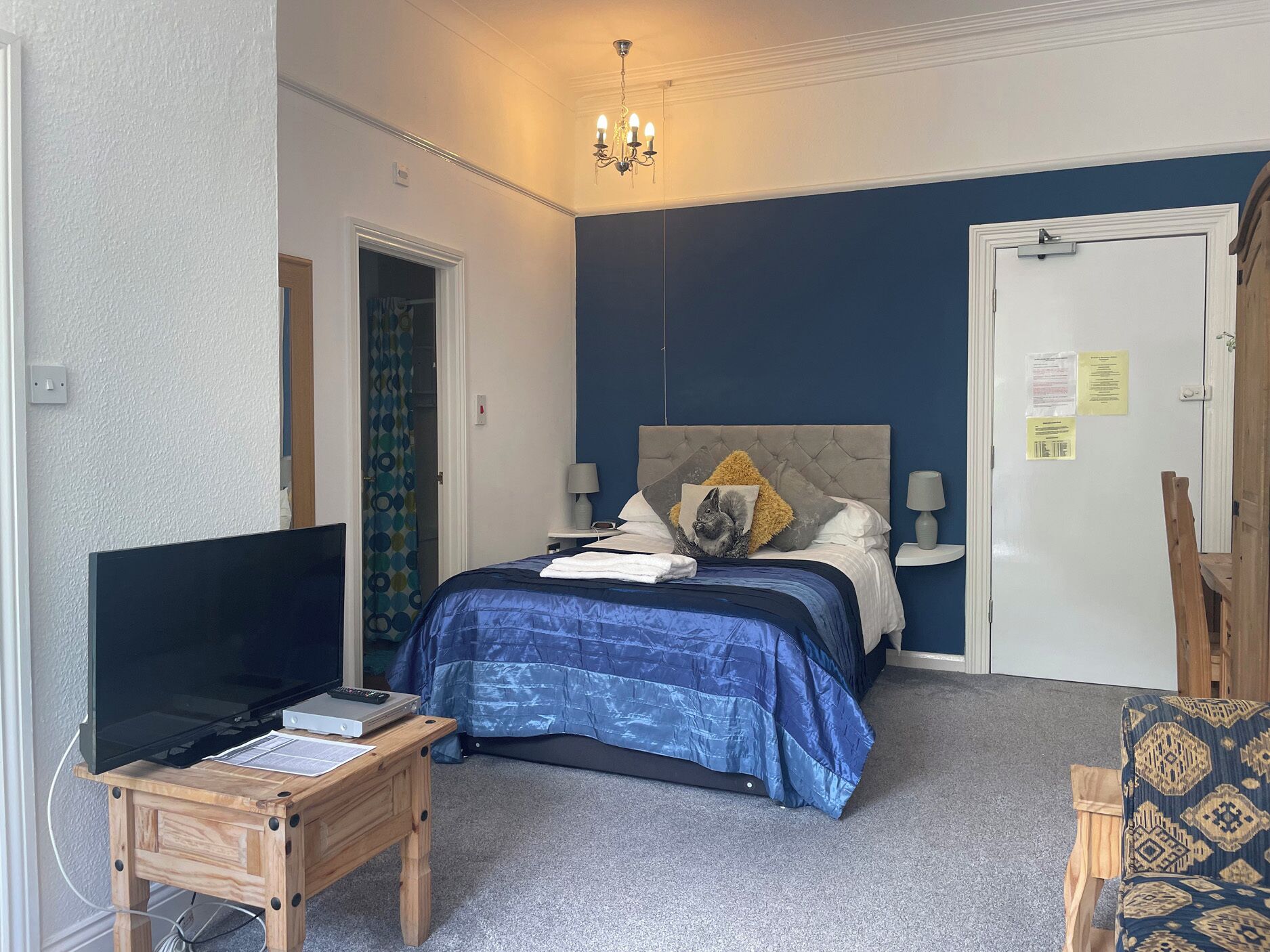 Ein Schlafzimmer mit Bett, Fernseher, Schreibtisch, Stuhl und einer Tür mit einem Hinweis.