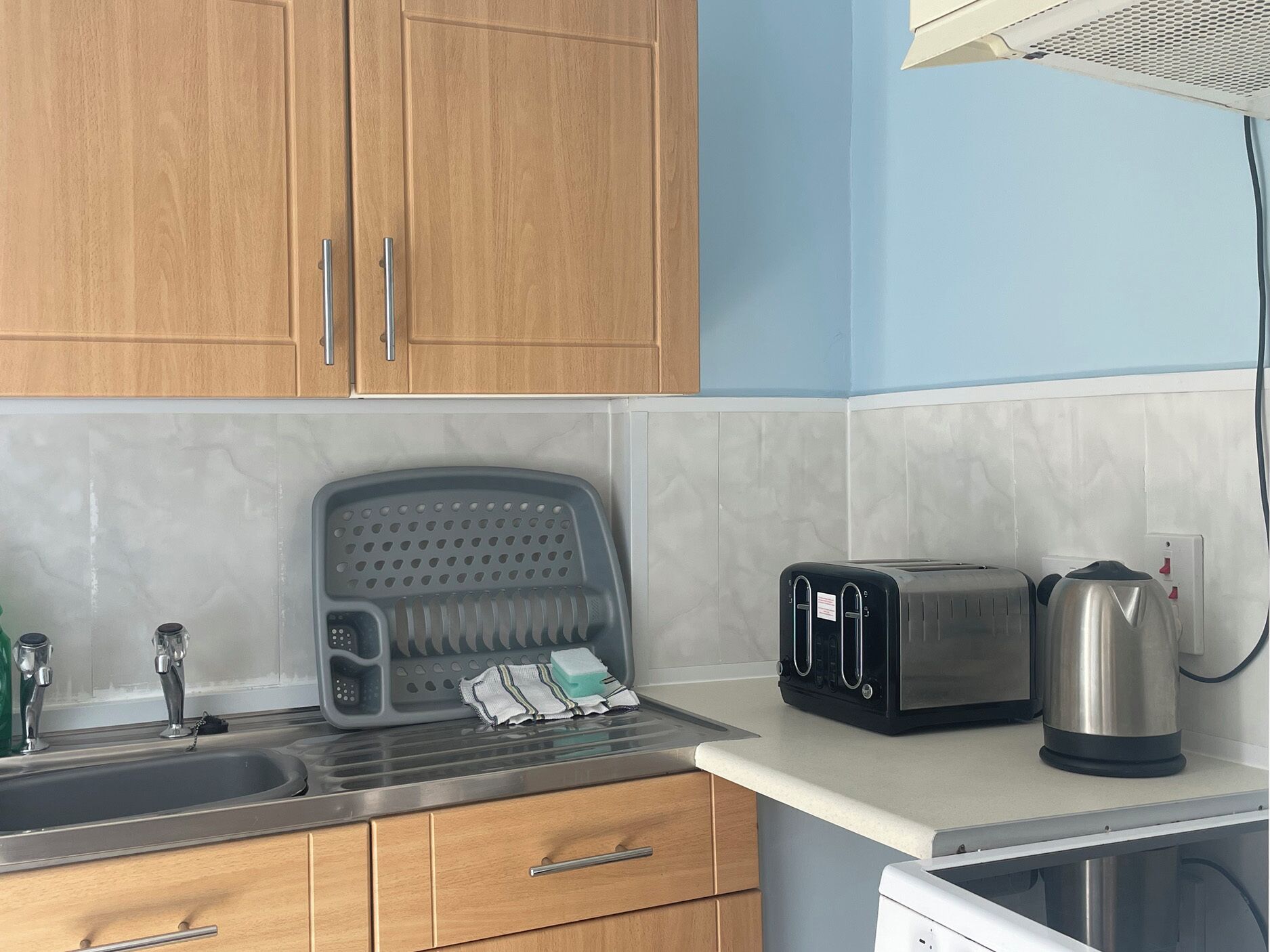 A kitchen with wooden cabinets, a stainless steel sink, a toaster, a kettle, and a microwave.