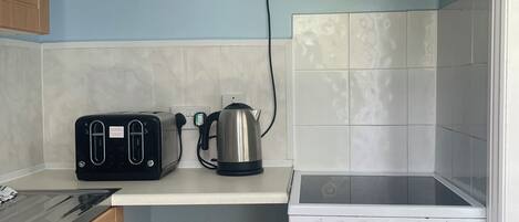 Une petite cuisine équipée d’un grille-pain noir, d’une bouilloire et d’une cuisinière blanche.