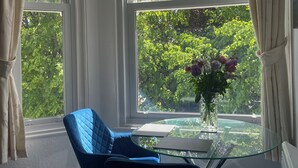 A room with a round glass table, a blue chair, and a vase with flowers. - Apartment 6 (Torquay)