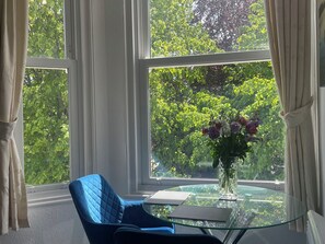 Ein Zimmer mit einem runden Glastisch, einem blauen Stuhl und einer Vase mit Blumen.