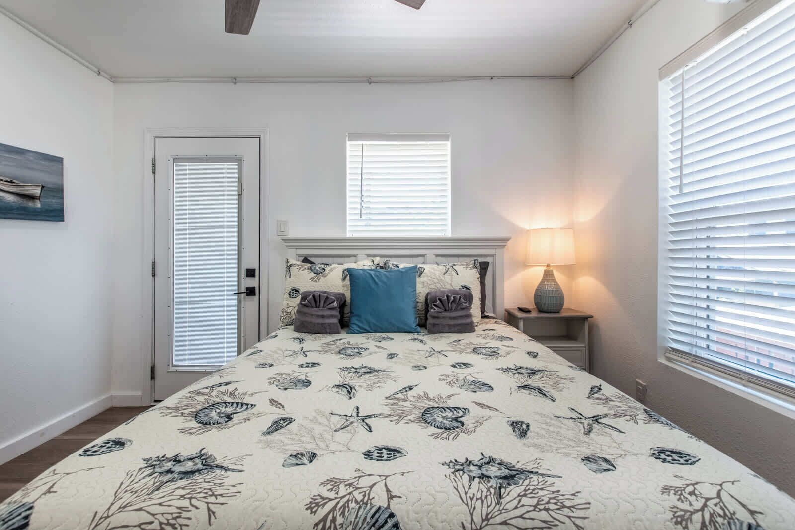 Un dormitorio con una cama, una mesita de noche, una lámpara, una puerta y una ventana con persianas.