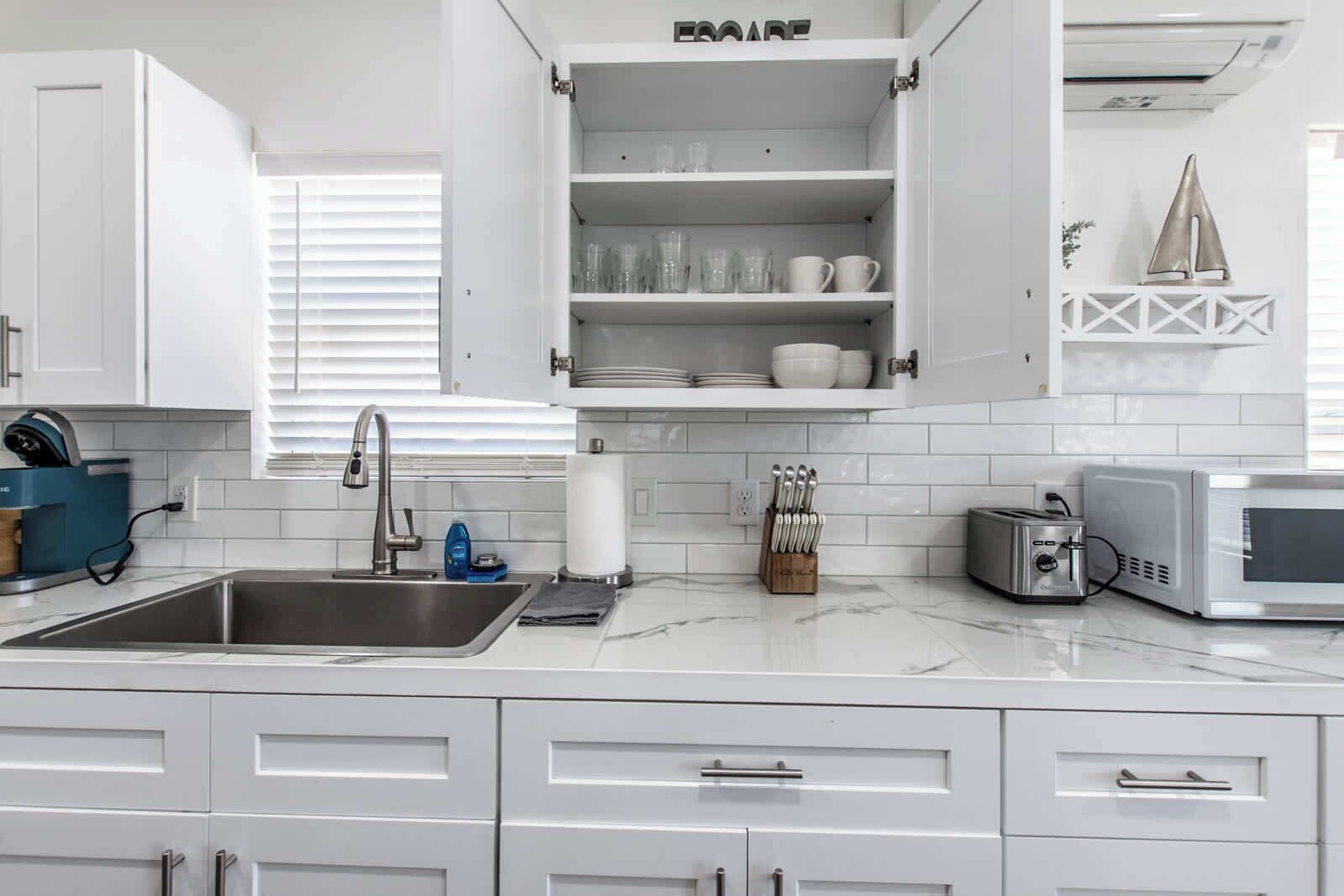 A modern kitchen with white cabinets, a stainless steel sink, a built-in microwave, and a toaster.