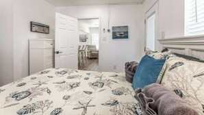 Een slaapkamer met een bed, een kaptafel, een stoel en een deur naar een andere kamer.